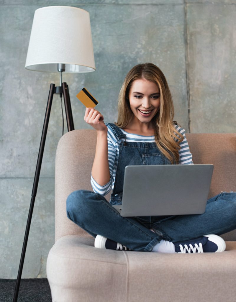 happy-beautiful-woman-holding-credit-card-in-hand-and-sitting-on-sofa-with-laptop.jpg